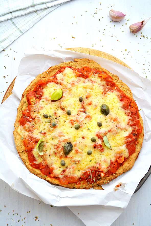 Home-made cauliflower-crust pizza with tomato sauce, melted mozzarella, capers and basil on parchment paper